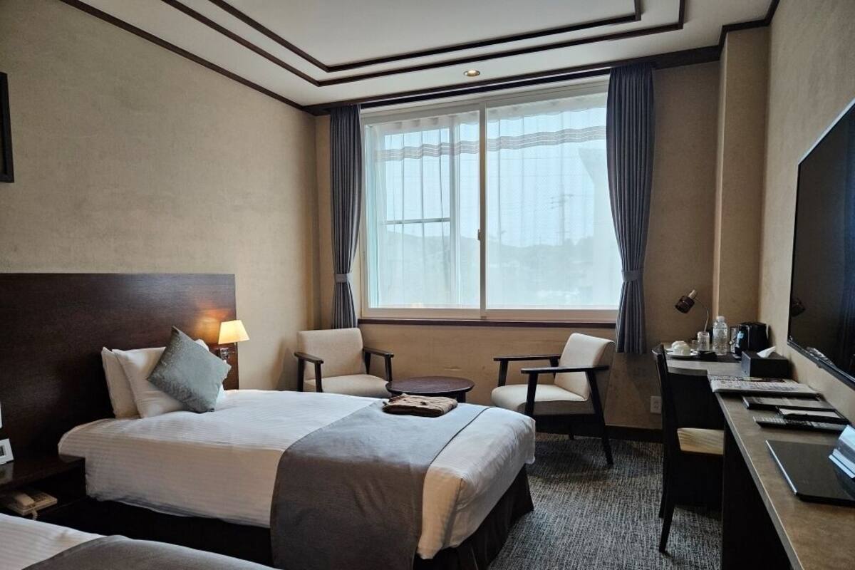 Une chambre d’hôtel avec deux lits, un bureau, une chaise, une télévision et une fenêtre avec des rideaux.