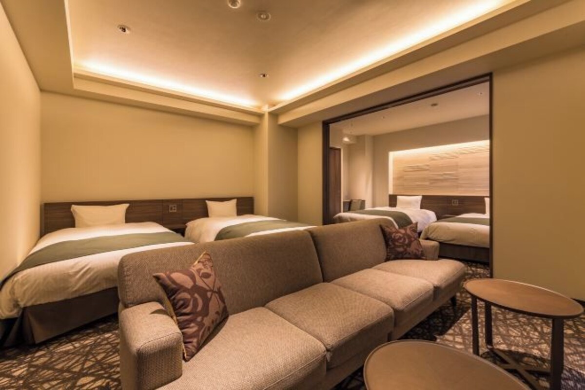 Habitación de hotel con dos camas, un sofá, una pequeña mesa y un espejo.