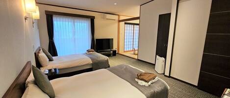 A hotel room with two beds, a desk, a chair, a TV, and a wardrobe.