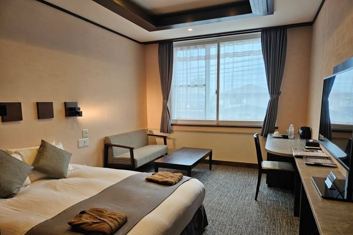 Une chambre d’hôtel avec un grand lit, un bureau, une chaise, un canapé et une fenêtre avec des rideaux.
