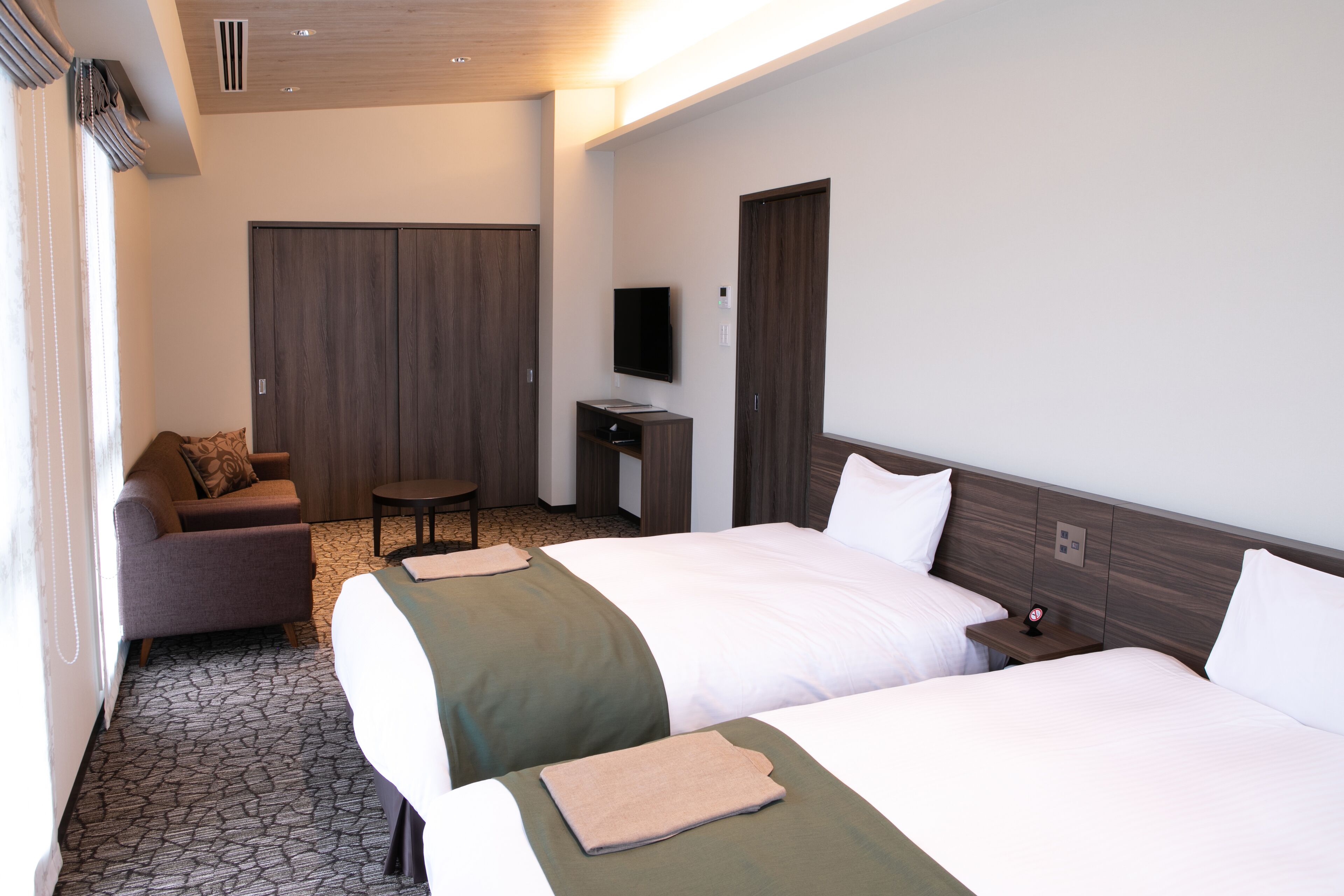 A hotel room with two beds, a sofa, a TV, and a wardrobe.