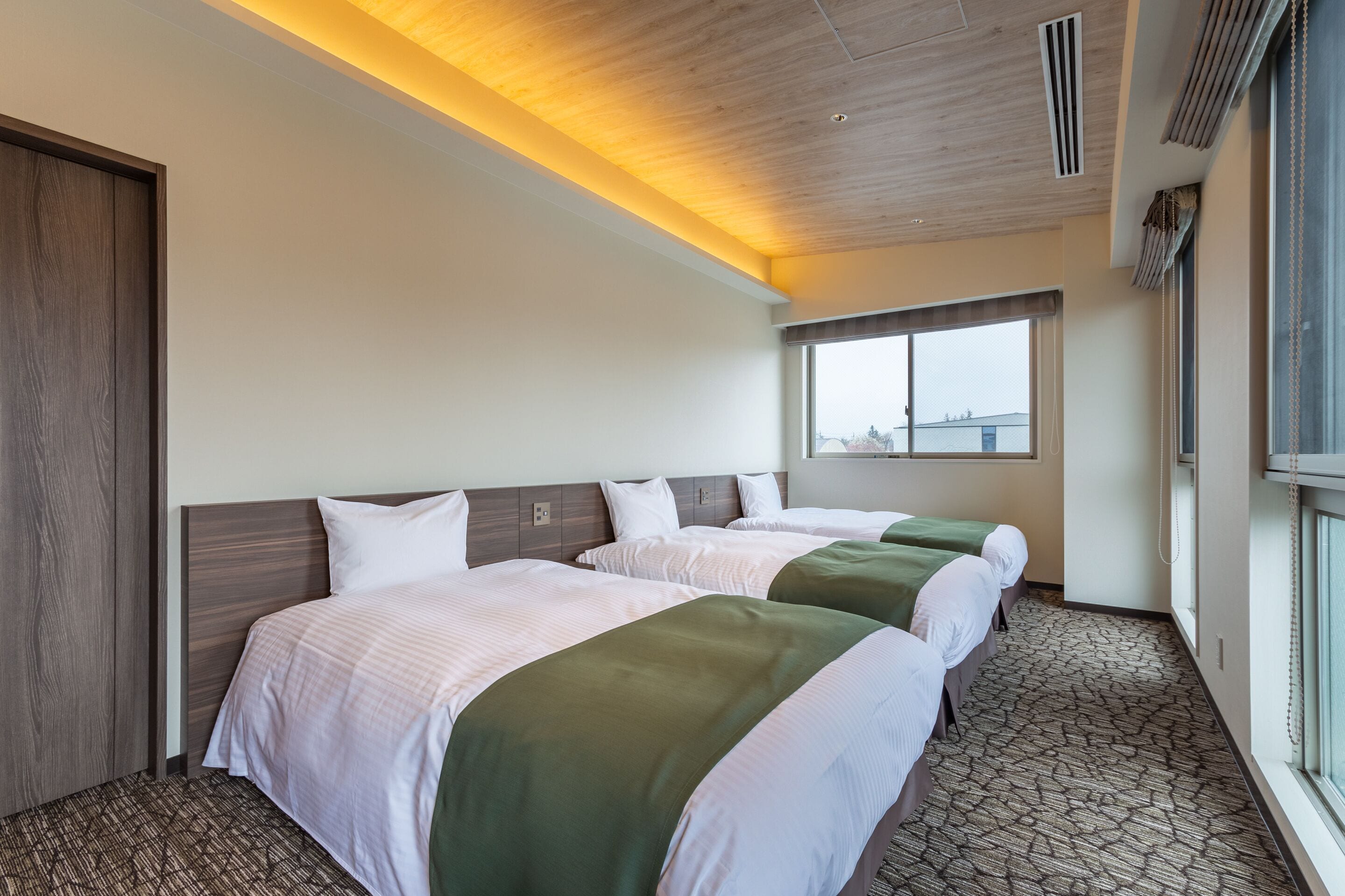 A hotel room with two beds, a large window, and a patterned carpet.