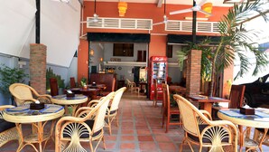 An outdoor dining area with wicker furniture and a brick wall. - Cheng Lay Guesthouse (Siem Reap)