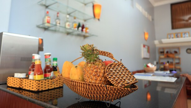 A reception area with a wicker fruit basket on the counter, a glass shelf with bottles, and a wall-mounted clock. - Cheng Lay Guesthouse (Siem Reap)