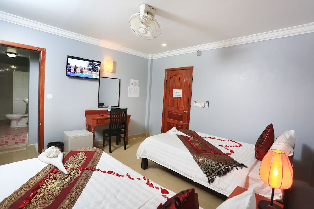 Quarto de hotel com duas camas, uma escrivaninha, uma cadeira, uma televisão e um abajur.