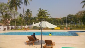 A swimming pool with lounge chairs and umbrellas, surrounded by palm trees and greenery. - Myanmar Sports Hotel (Yangon)