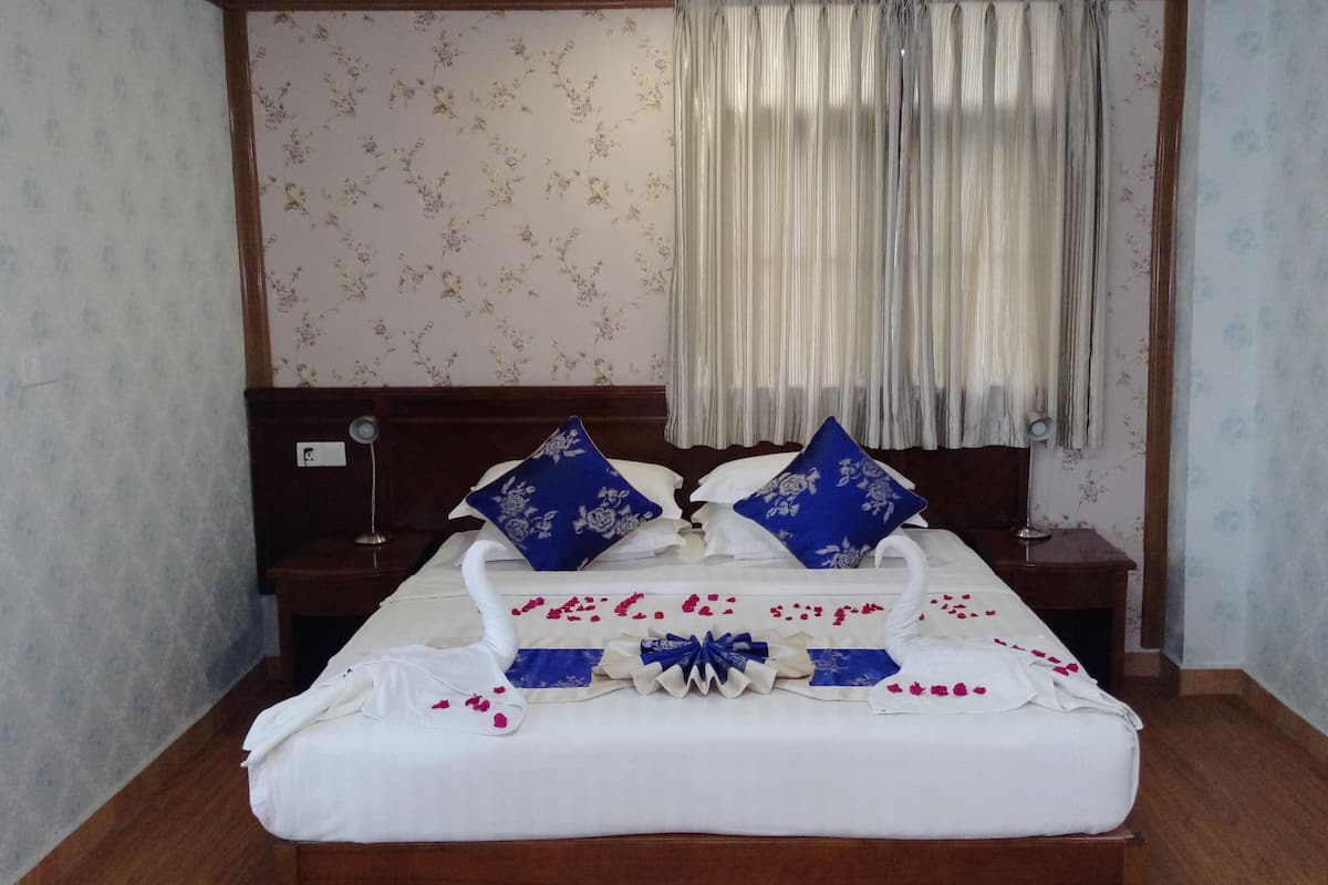 Een net opgemaakt bed met witte lakens en blauwe kussens met bloemenprint, een houten hoofdbord en een nachtkastje met een lamp.