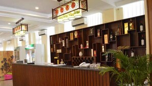 A reception desk with a wooden finish, a potted plant, and a wine rack with bottles. - Myanmar Sports Hotel (Yangon)