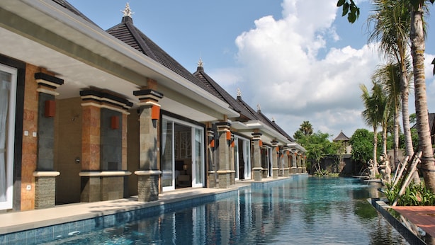 Une piscine au design moderne, entourée d’une rangée de bâtiments aux éléments architecturaux traditionnels.