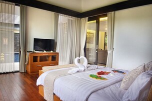 A hotel room with a large bed, a wooden dresser, a television, and a balcony with curtains.