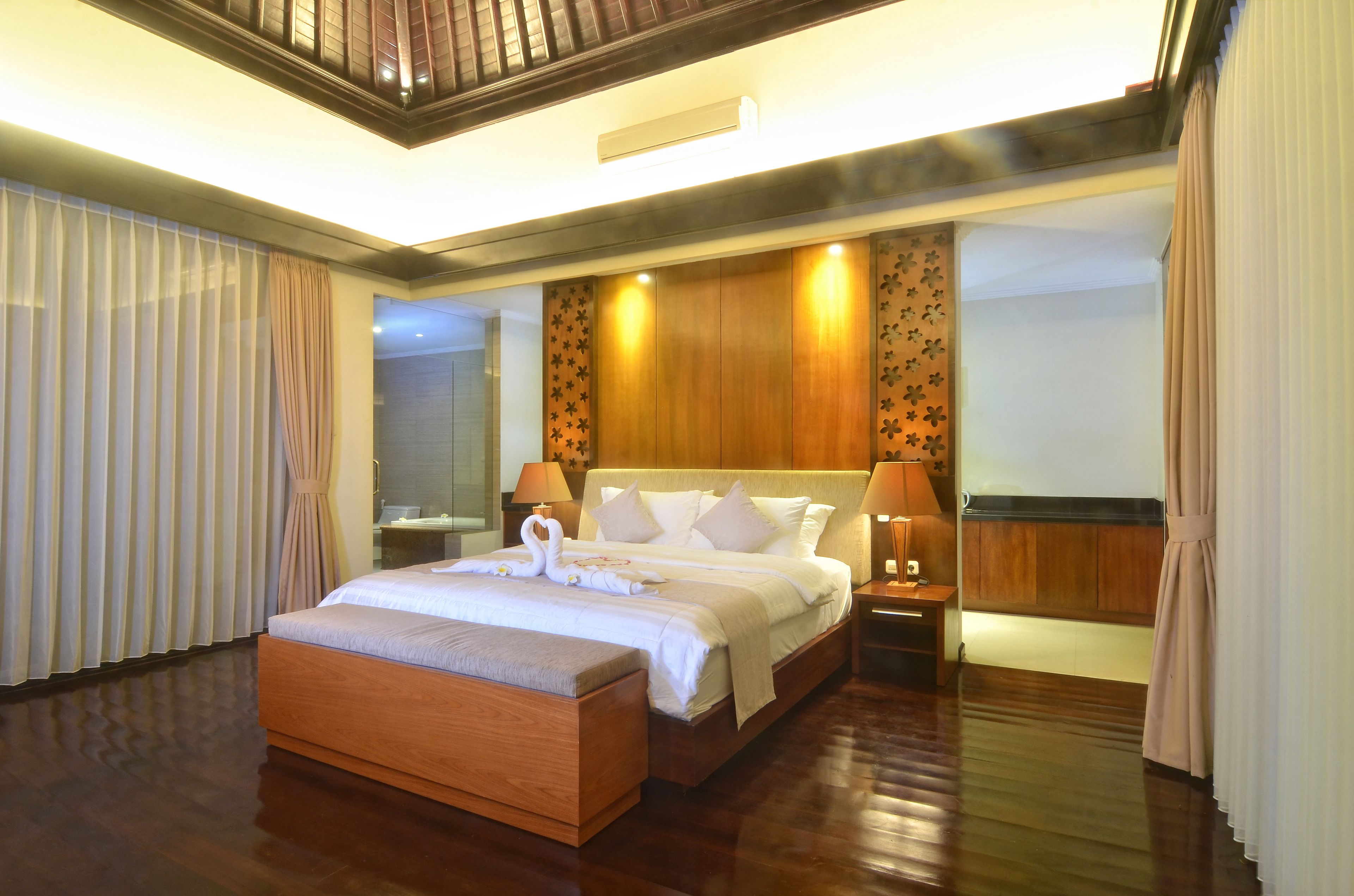 Una habitación de hotel espaciosa con una cama grande, cabecero de madera y una mesita de noche con lámpara.