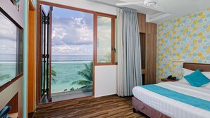 Habitación de hotel con un amplio ventanal corredizo hacia el océano, una cama con almohada azul y un muro con diseño.