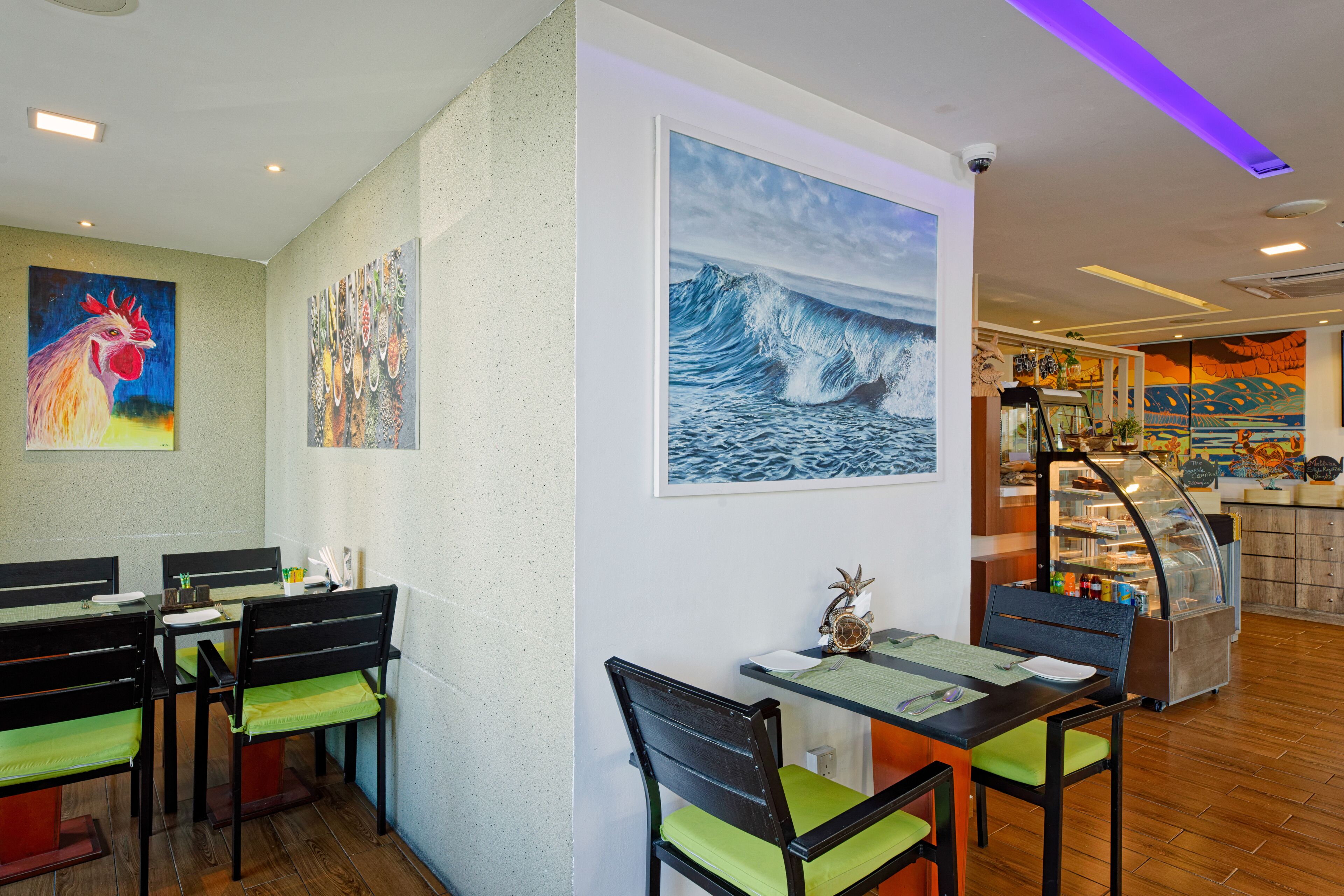 A restaurant with a dining area featuring tables and chairs, a counter with a display case, and wall art.
