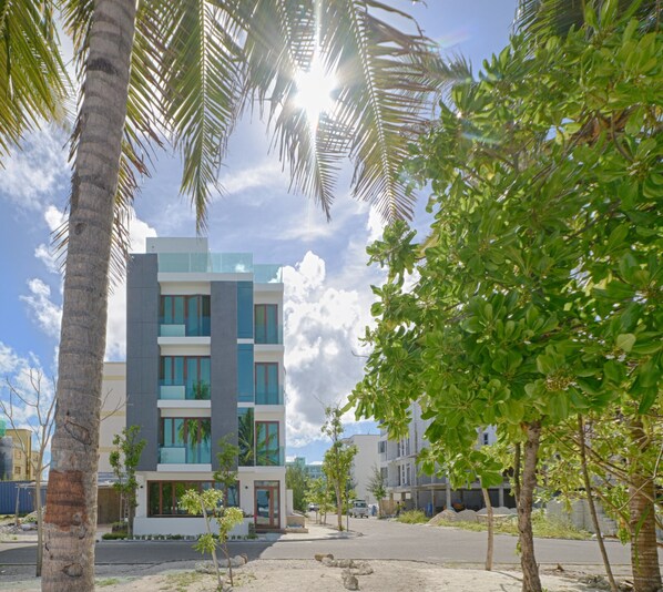 A modern multi-story building with large windows and a flat roof, surrounded by palm trees and greenery.