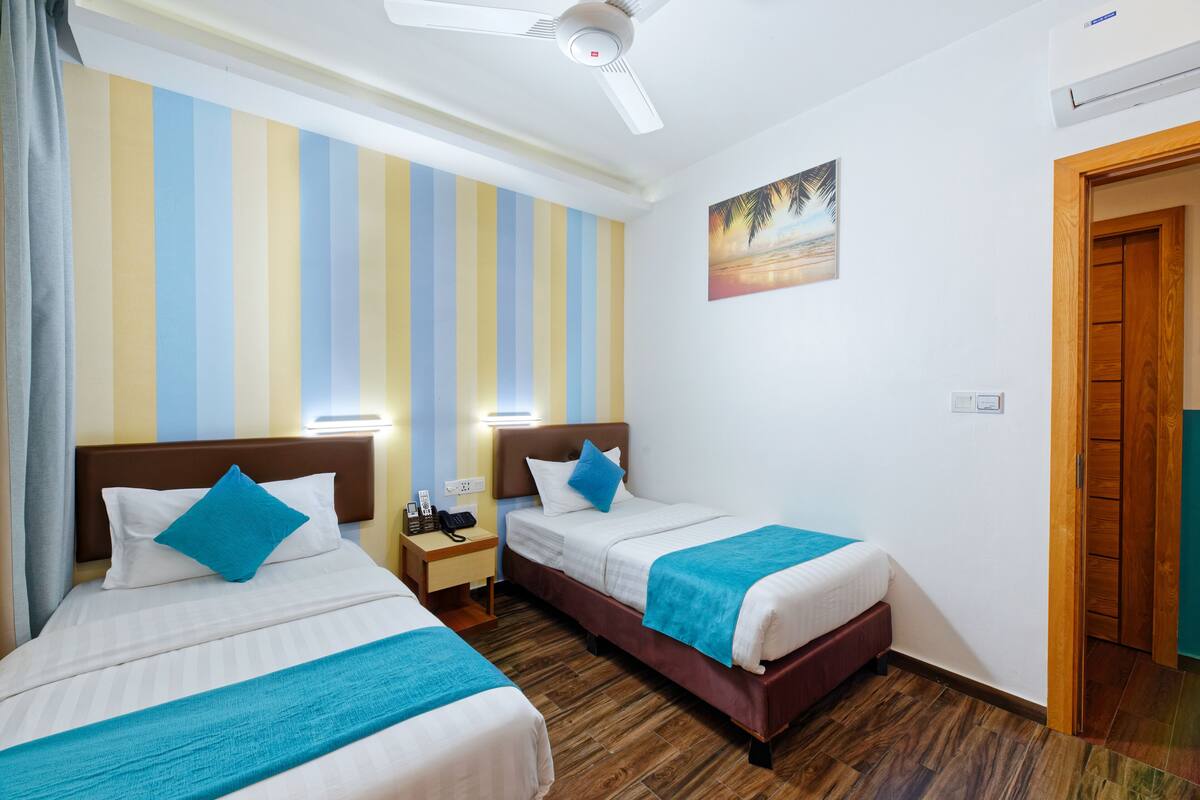 A hotel room with two beds, striped wall decor, a painting, and a ceiling fan.