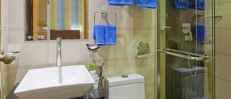 Un baño moderno con lavamanos blanco, tocador negro y cabina de ducha de vidrio.
