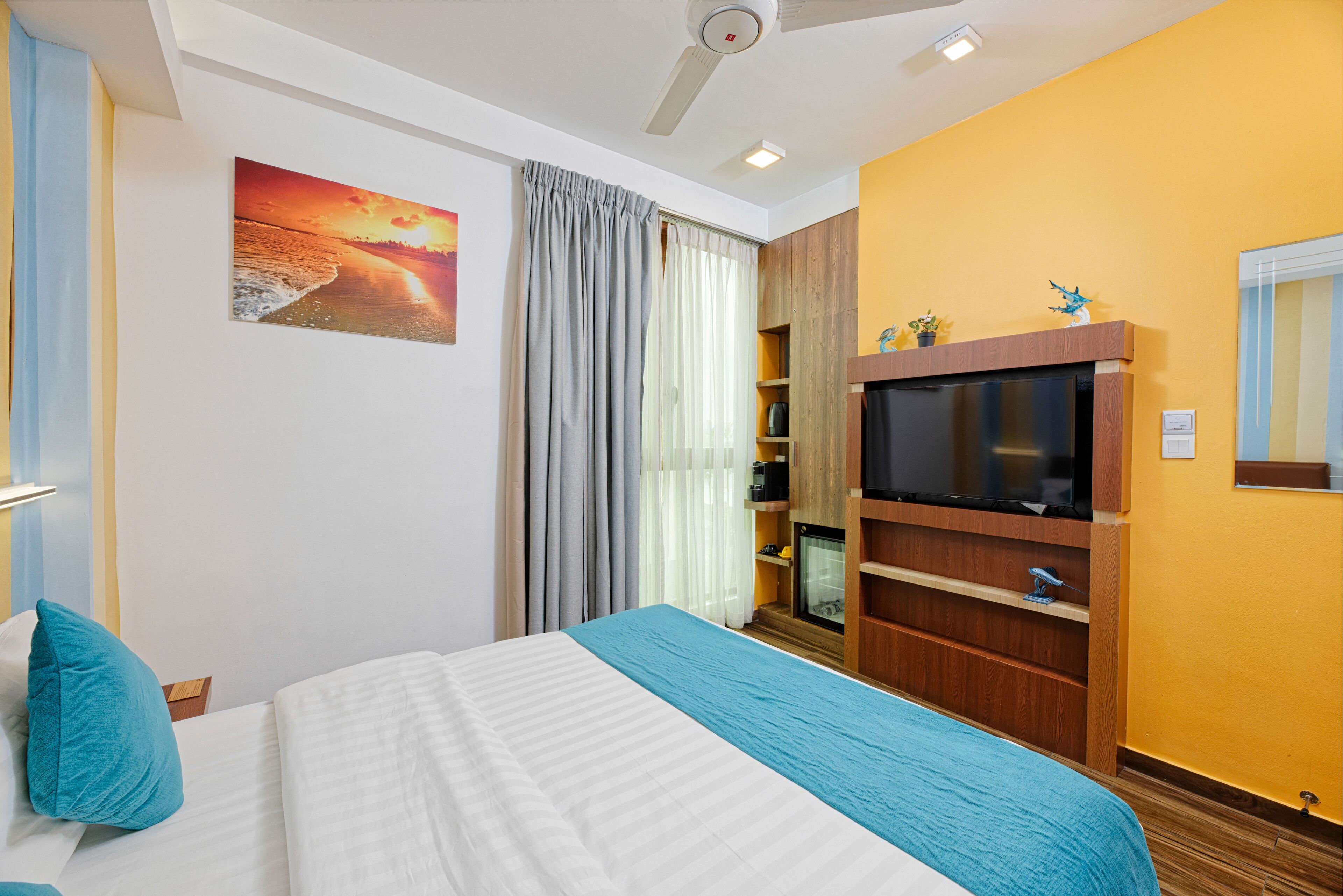 Une chambre d’hôtel avec un lit, un téléviseur à écran plat, un meuble de rangement en bois et un tableau au mur.