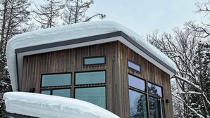 A modern wooden house with large windows and a covered porch, surrounded by snow and trees. - Morino Lodge Chalets (Hakuba)