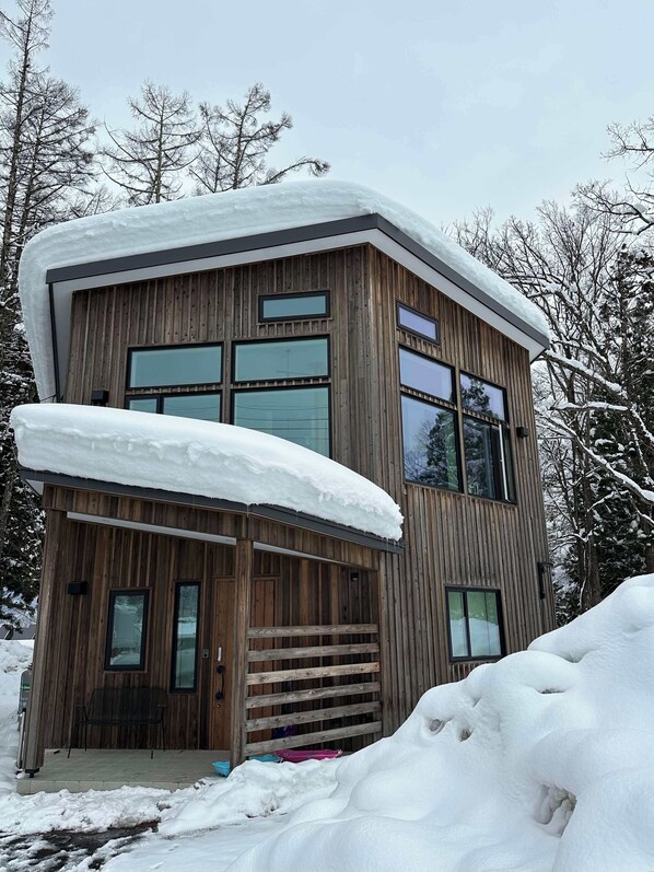 A modern wooden house with large windows and a covered porch, surrounded by snow and trees. - Morino Lodge Chalets (Hakuba)