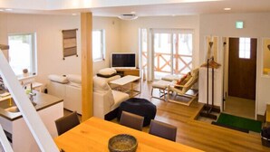 A spacious loft-style room with a wooden dining table, a sofa, and a TV. - Morino Lodge Chalets (Hakuba)