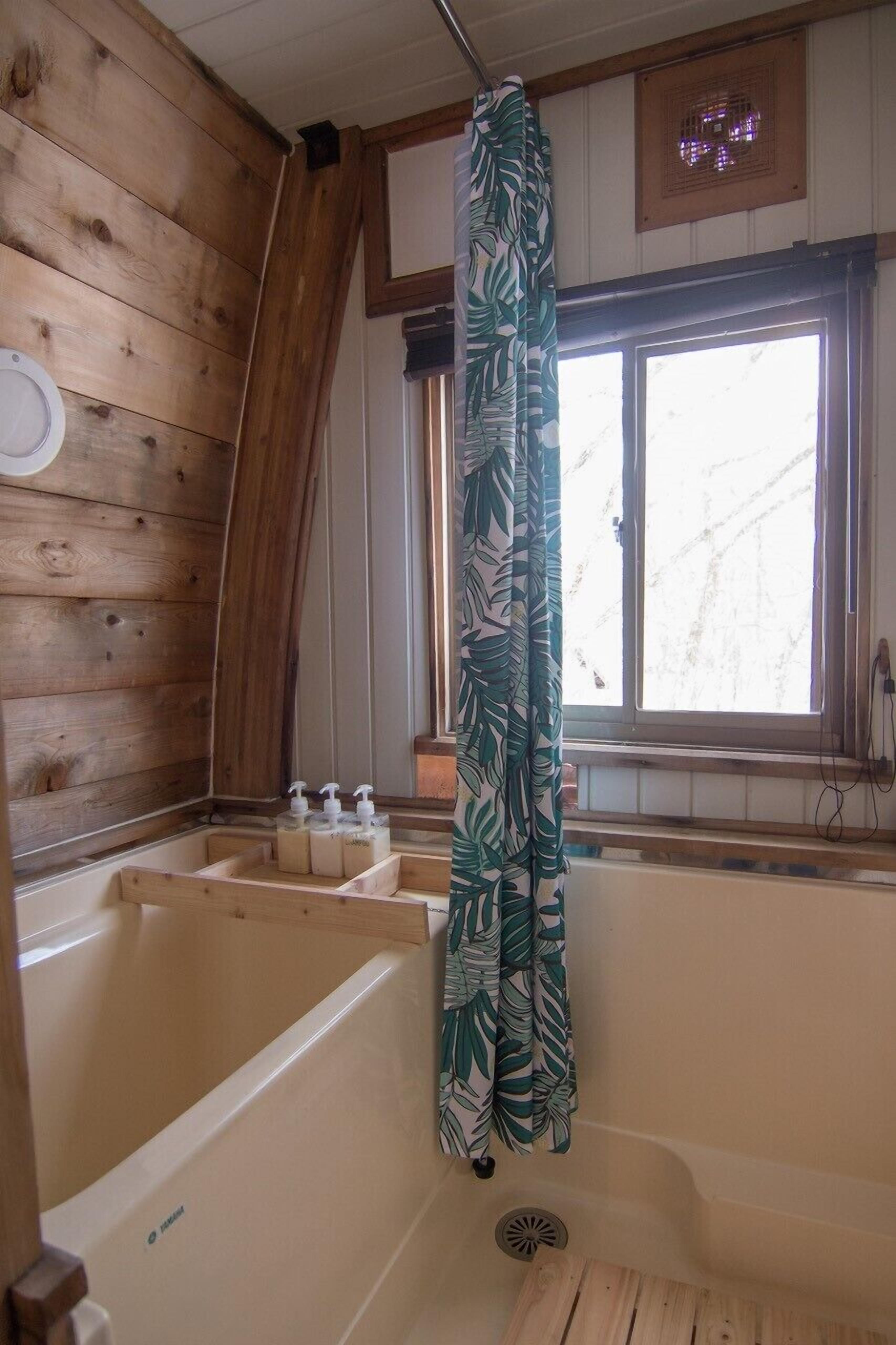 A wooden cabin bathroom with a bathtub, a window, and a shower curtain.