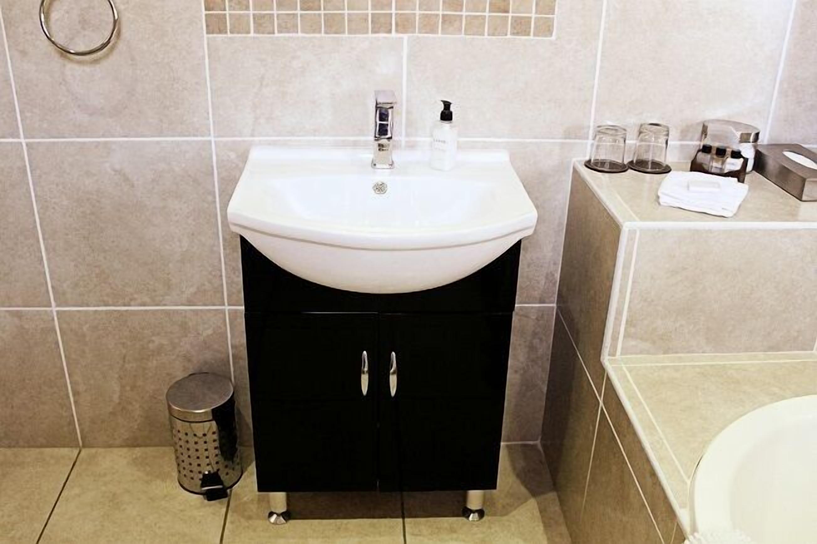 A bathroom with a white sink, black cabinet, and a small trash can.