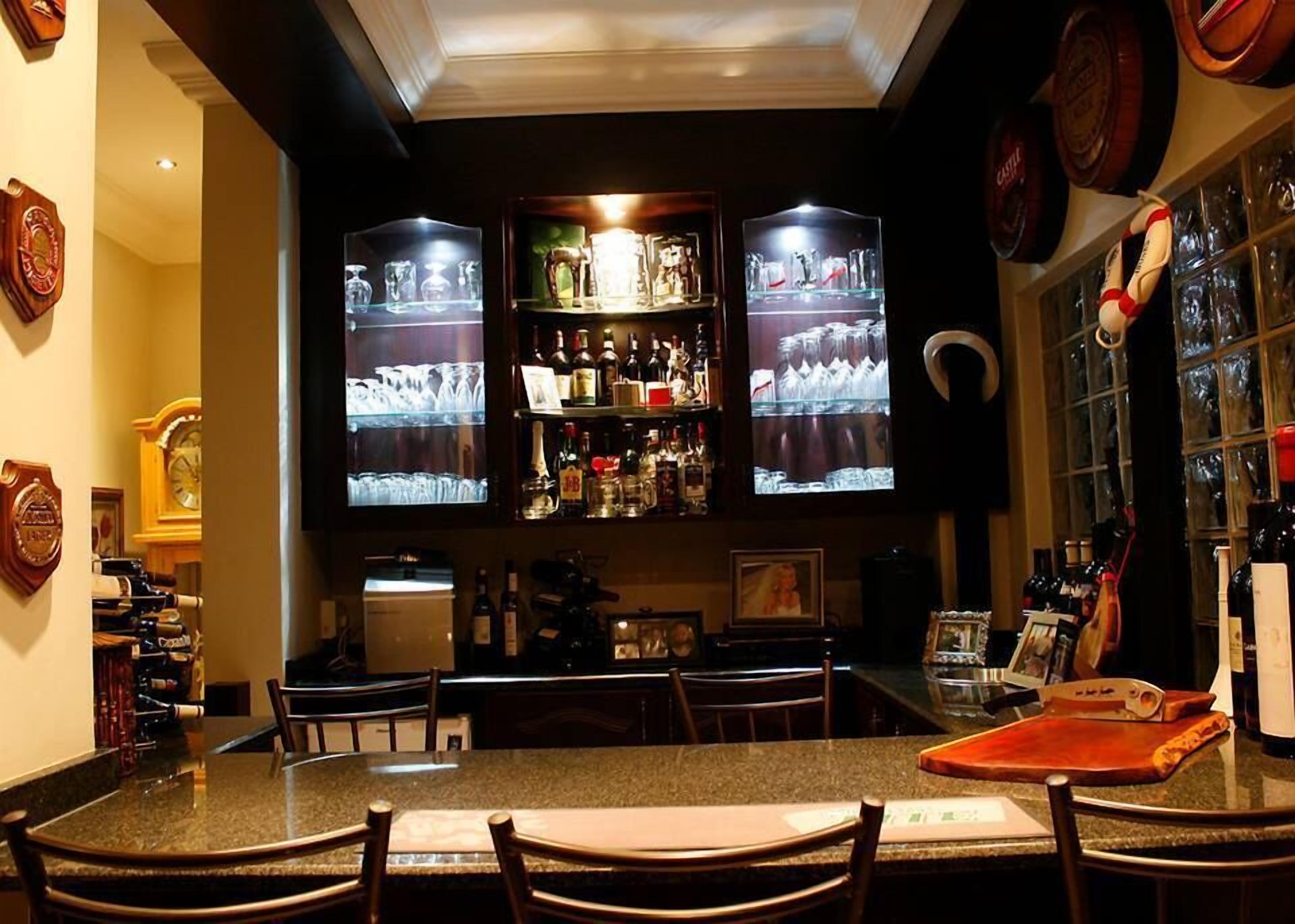 Zona de bar con varias televisiones mostrando deportes, barra provista de botellas y área de estar con sillas y una mesa.