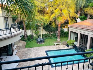 A residential backyard with a swimming pool, a dining area, and a covered patio.