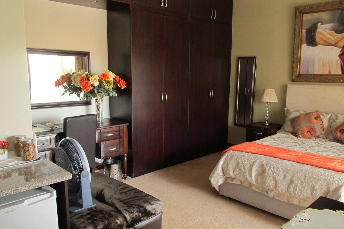 Ein Schlafzimmer mit einem Bett, einem Schreibtisch, einem Stuhl, einem Kleiderschrank und einem kleinen Tisch mit Blumen in einer Vase.