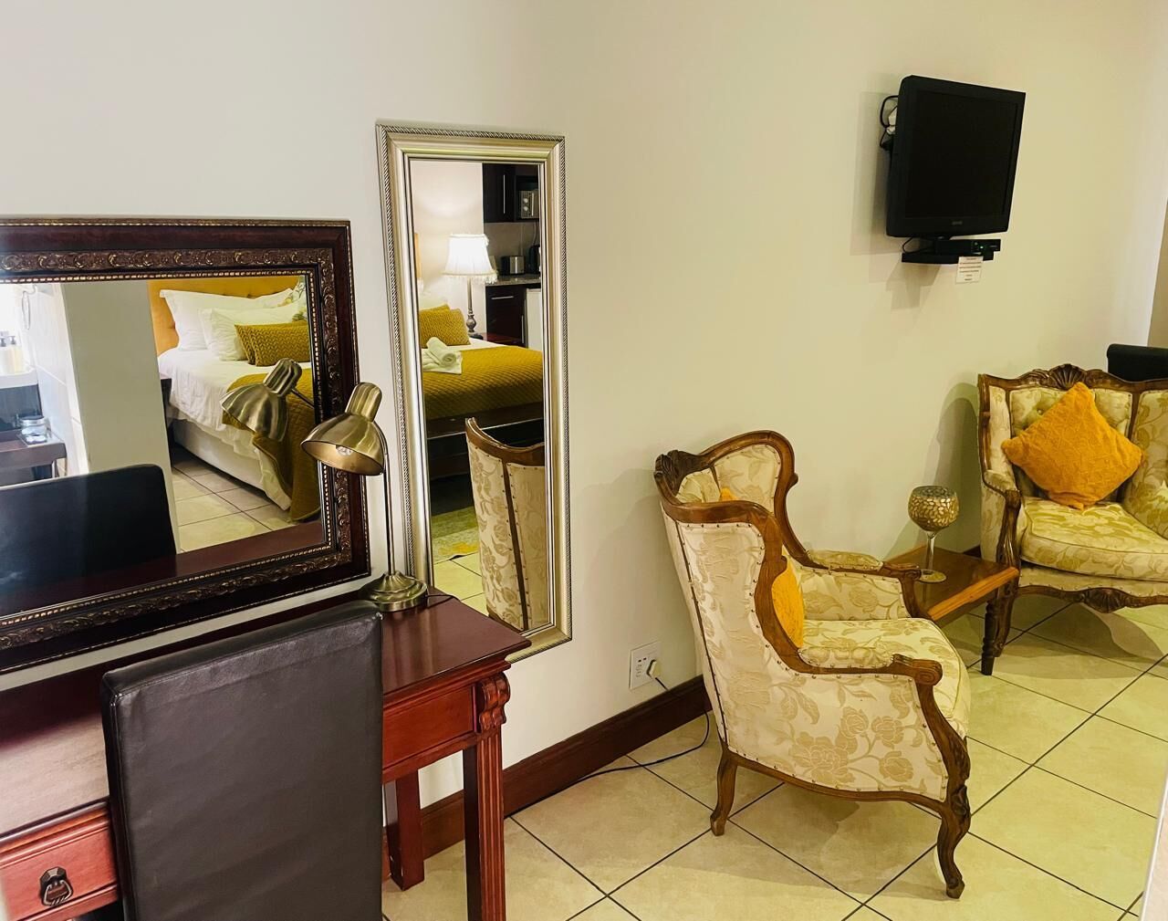 Una habitación con un espejo grande, un televisor montado en la pared y dos sillones tapizados con cojines.