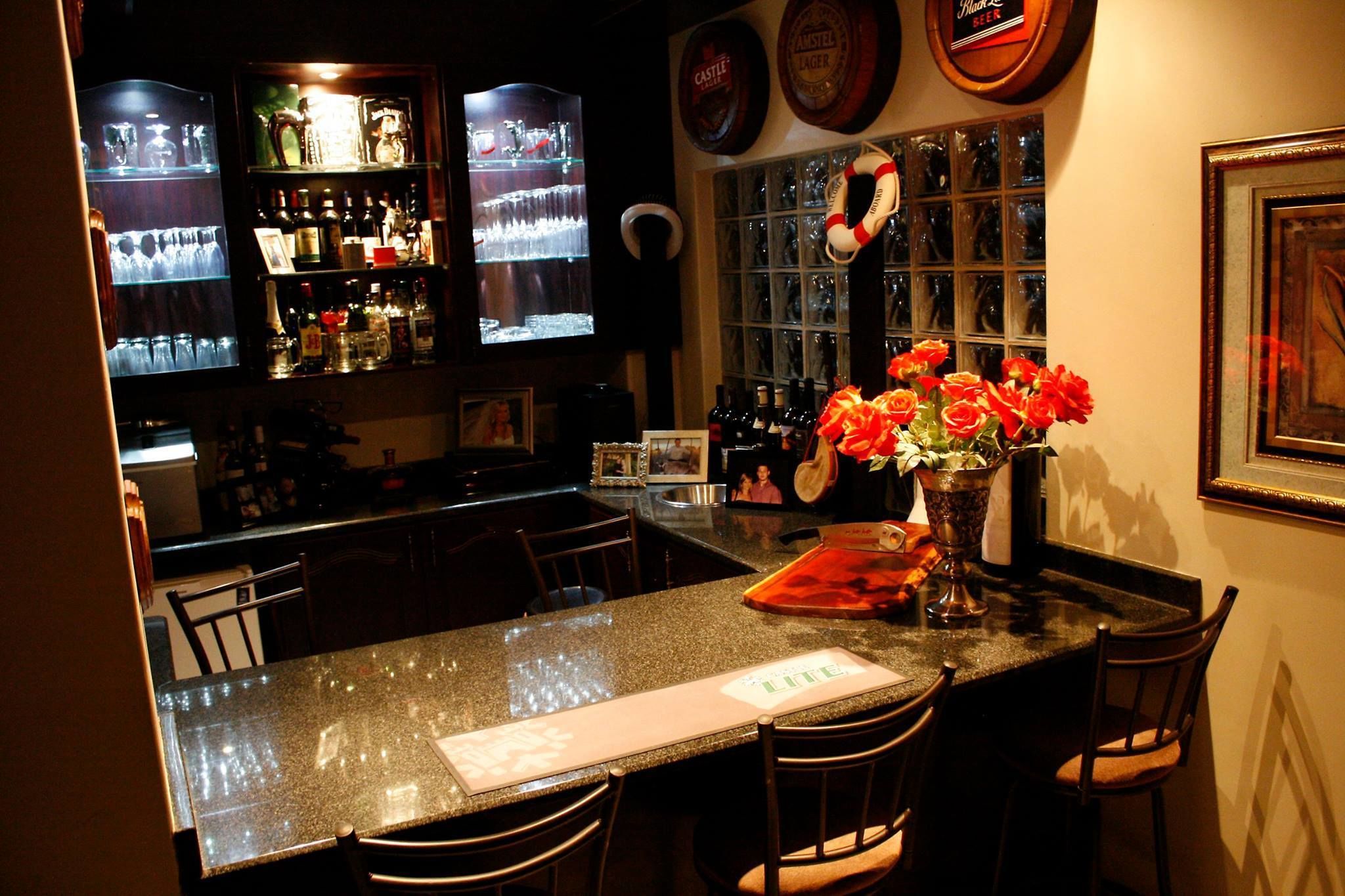 A bar area with a granite countertop, bar stools, and a vase of red flowers.