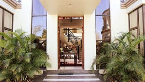 Une entrée moderne, avec un escalier menant à un balcon, le tout entouré d’une végétation luxuriante.