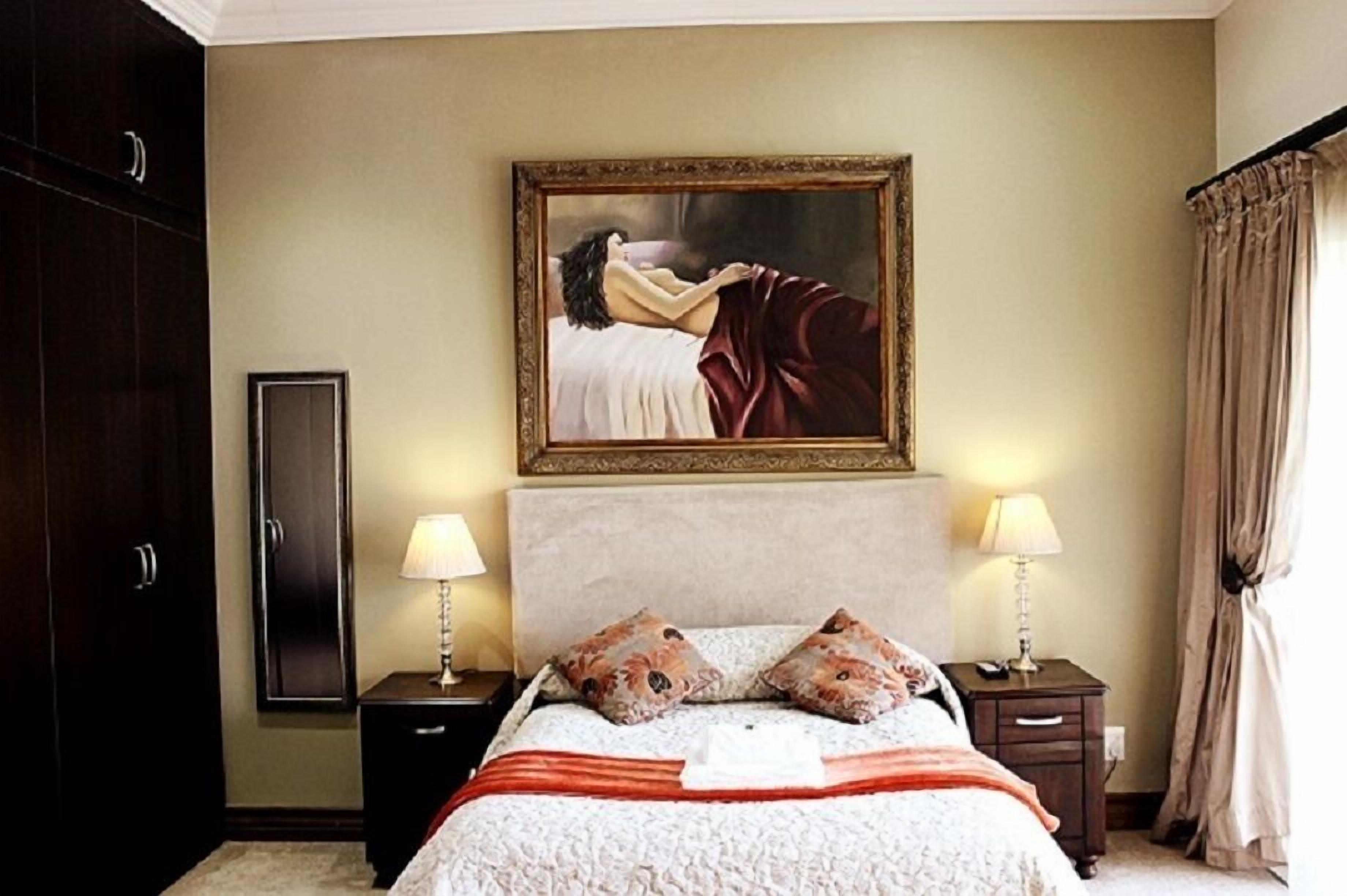 Habitación de hotel con una cama grande, dos mesitas de noche con lámparas, un armario y un cuadro en la pared.