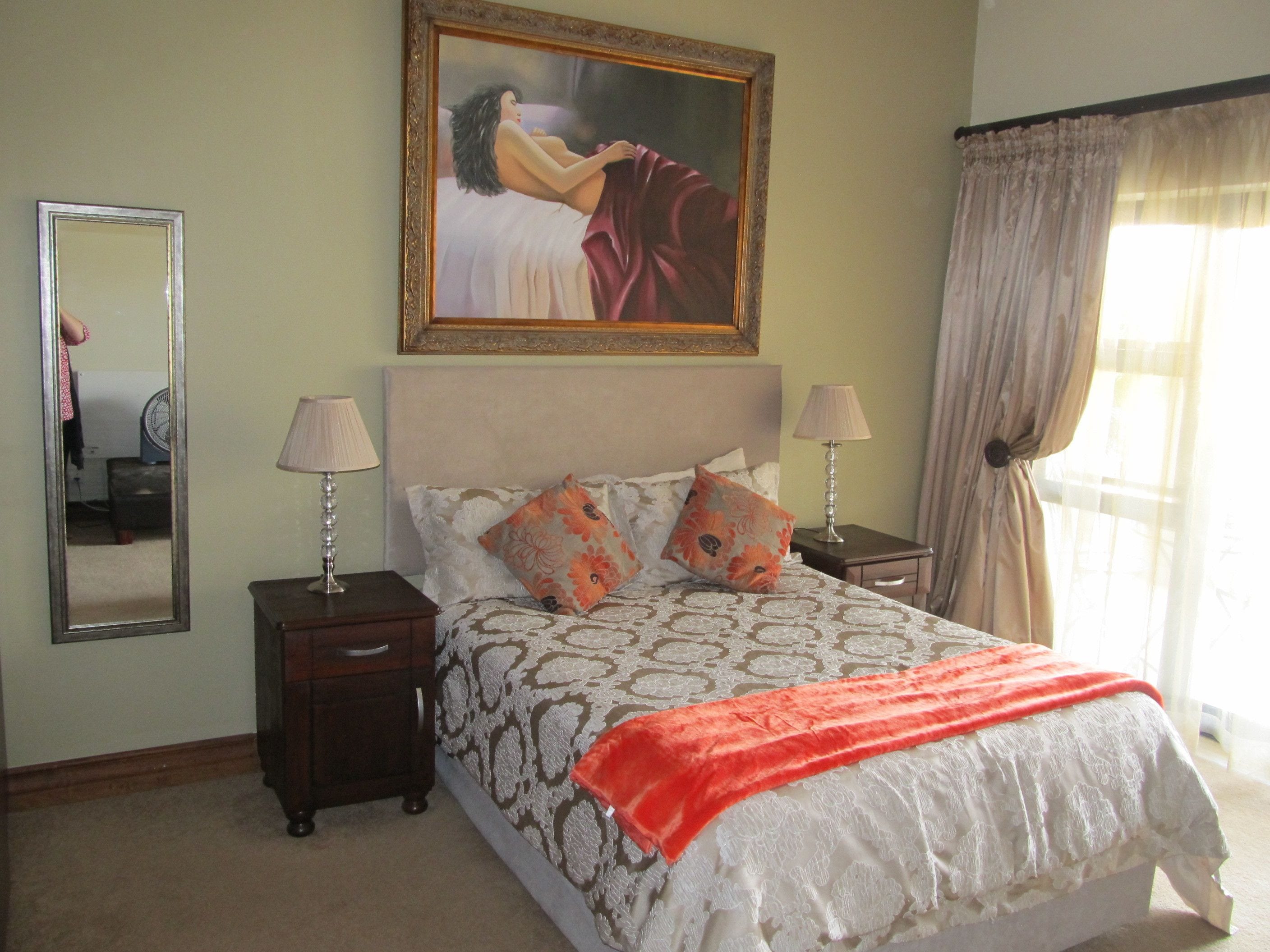 Une chambre à coucher bien rangée, avec un grand lit, deux tables de chevet, un miroir et un tableau accroché au mur.
