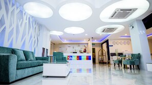 A modern hotel lobby with a reception desk, green sofas, and a tiled floor.