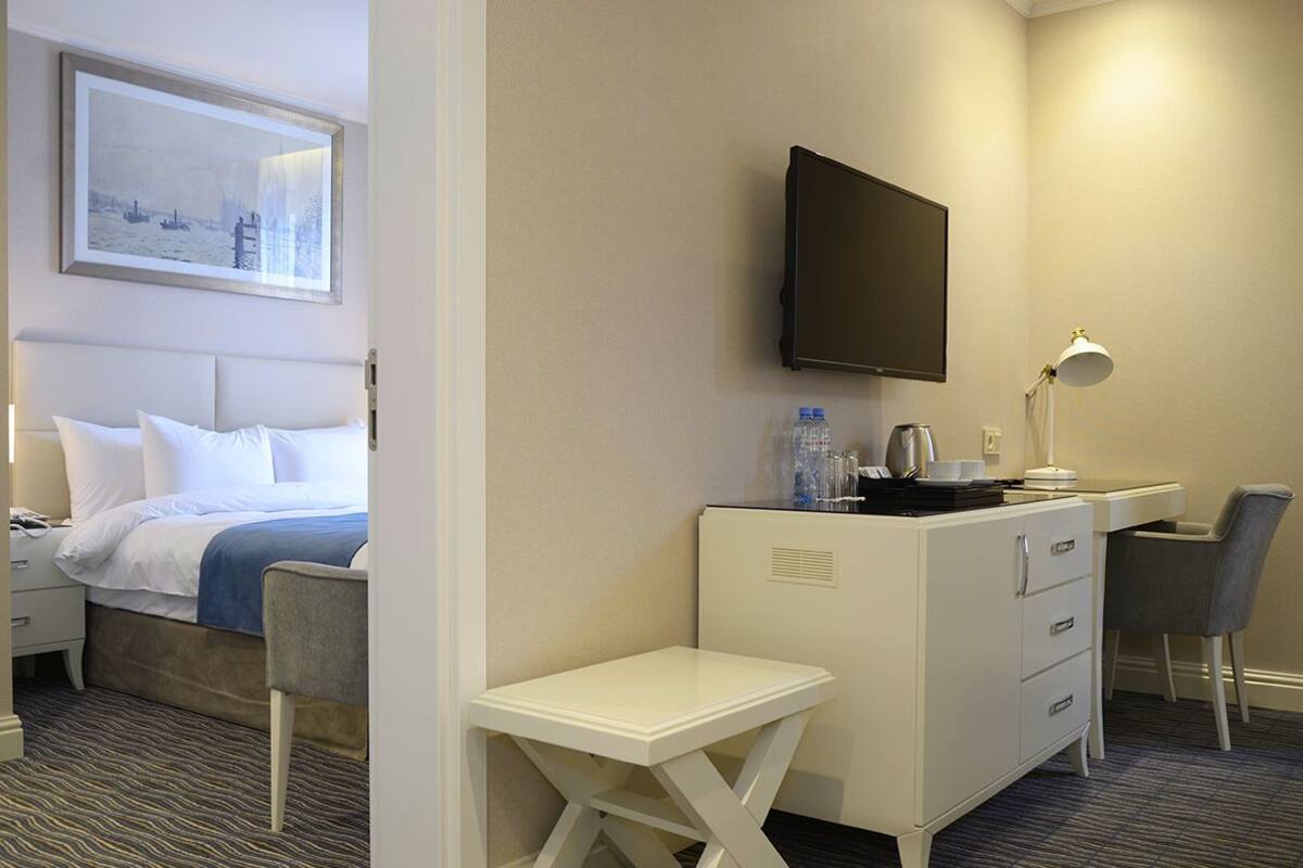 A hotel room with a bed, a desk, a chair, a TV, and a small table.