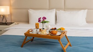 A neatly made breakfast tray on a bed with a blue bedspread, white pillows, and a beige headboard. - City Avenue (Tbilisi)