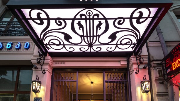 The City Avenue Hotel entrance with a decorative sign, wrought iron gates, and two potted plants. - City Avenue (Tbilisi)