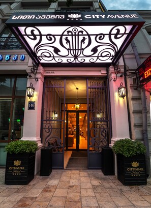 The City Avenue Hotel entrance with a decorative sign, wrought iron gates, and two potted plants. - City Avenue (Tbilisi)
