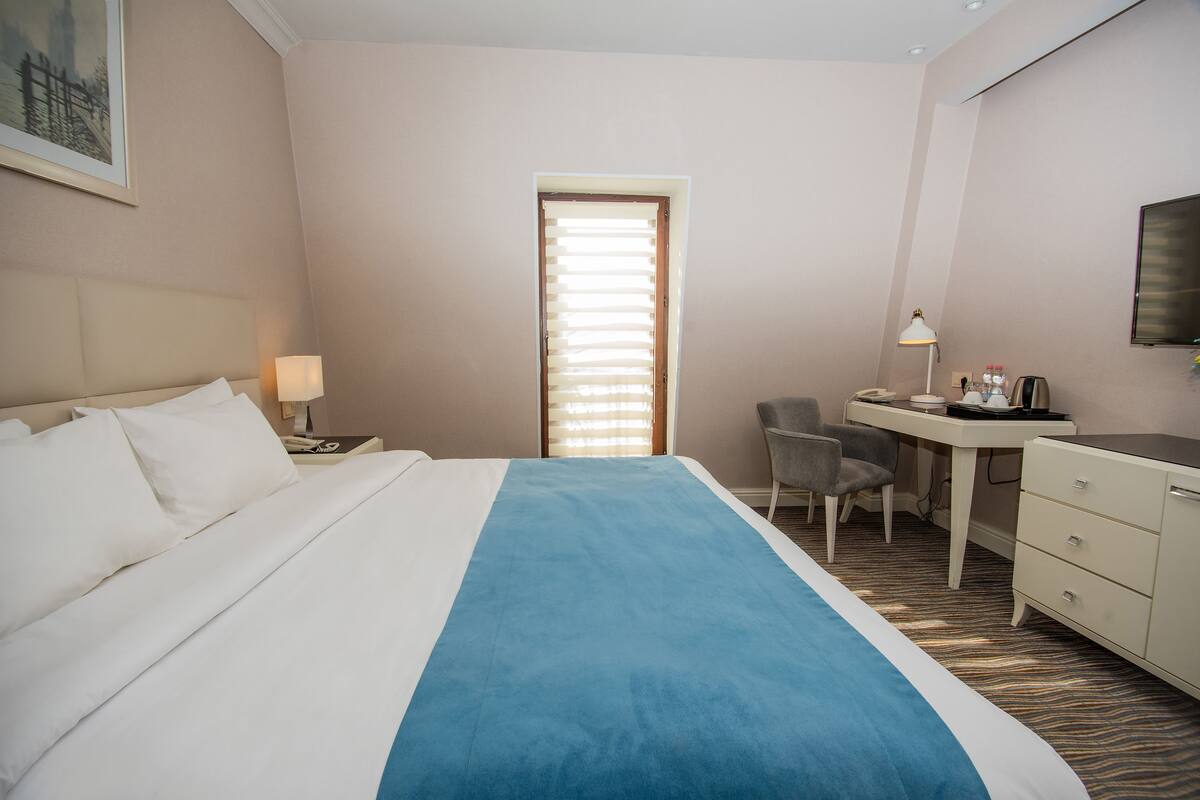 A hotel room with a bed, a desk, a chair, a desk lamp, and a television.