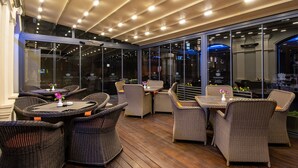 An outdoor seating area with wicker furniture and glass walls. - City Avenue (Tbilisi)