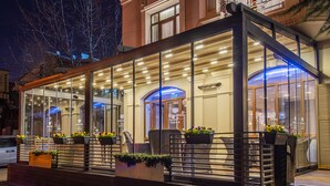 A glass-fronted building with outdoor seating and potted plants. - City Avenue (Tbilisi)