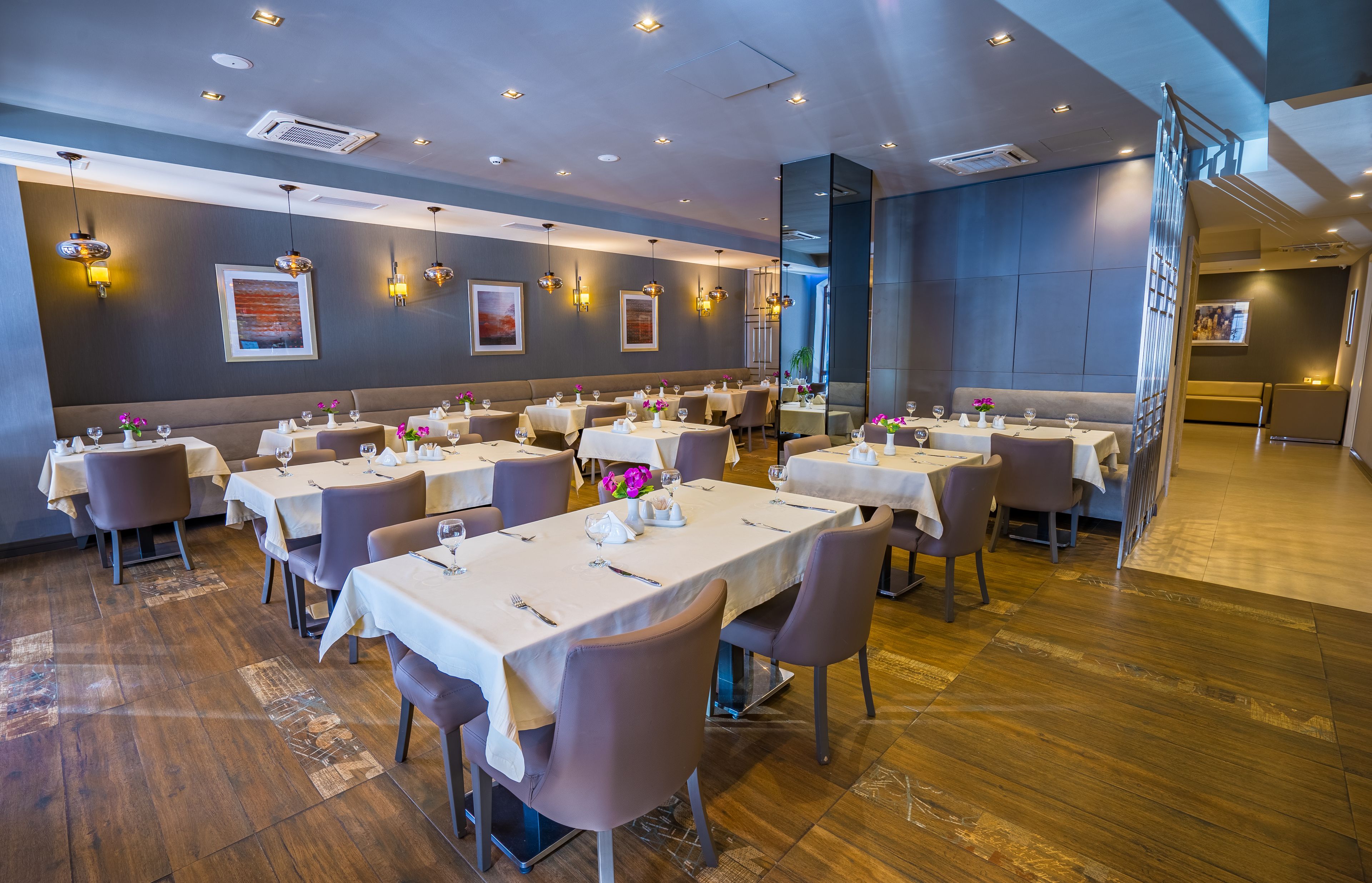 A restaurant with multiple tables, each set with white tablecloths and pink flowers.
