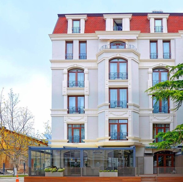A multi-story hotel with a classic architectural style, featuring a red roof, white facade, and multiple balconies with wrought iron railings. - City Avenue (Tbilisi)