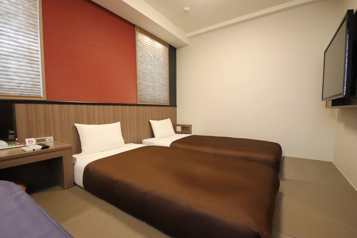 A hotel room with two beds, a wooden headboard, a desk with a phone and a radio, and a TV mounted on the wall.