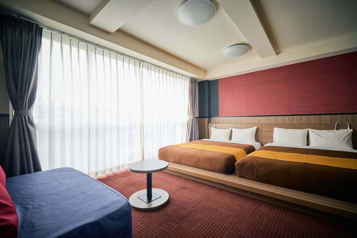 A hotel room with two beds, a round table, and a large window with curtains.