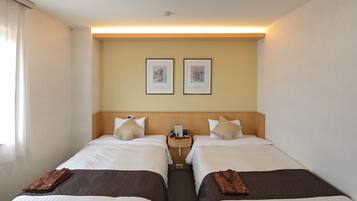 A hotel room with two single beds, a bedside table with a lamp, a wall-mounted phone, and two framed pictures above the beds.