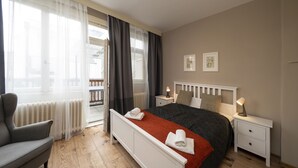 A bedroom with a bed, bedside tables, a chair, and a view of the outside. - New Town - Apple Apartments (Prague)