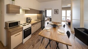 A modern kitchen with wooden cabinets, a dining table set for four, and a black leather couch in the dining area. - New Town - Apple Apartments (Prague)