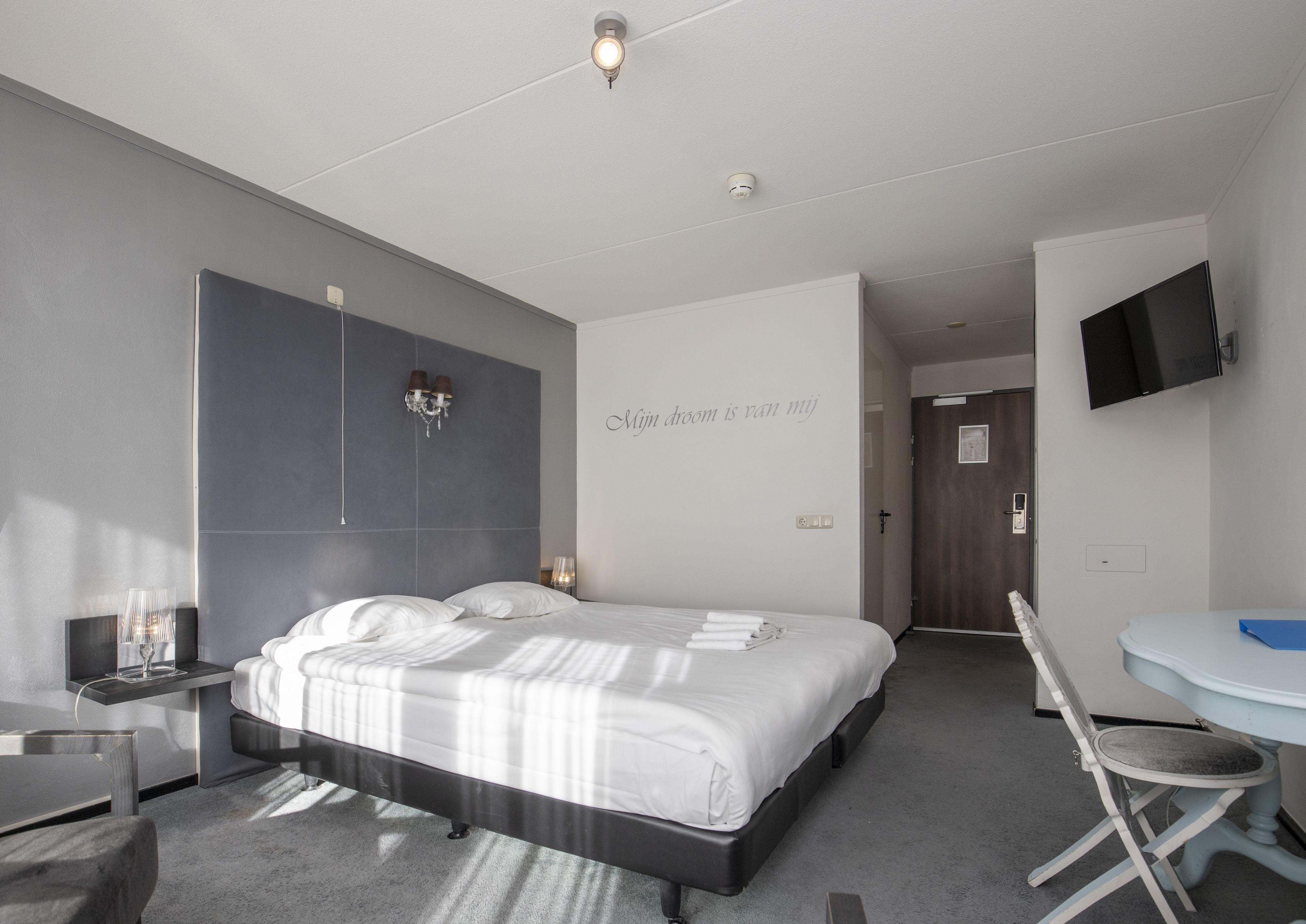 Habitació d'hotel moderna amb un llit gran, una taula de nit i un escriptori amb una cadira.